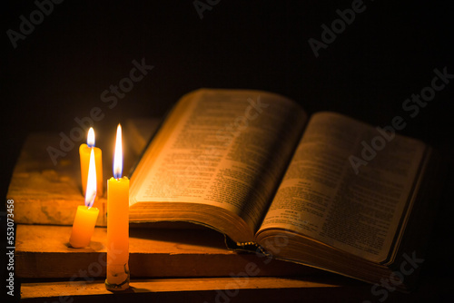 Fototapet Light candle with holy bible and cross or crucifix on old wooden background in church