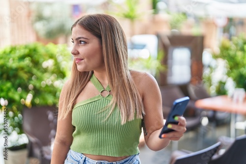 Young beautiful hispanic woman smiling confident using smartphone at coffee shop terrace