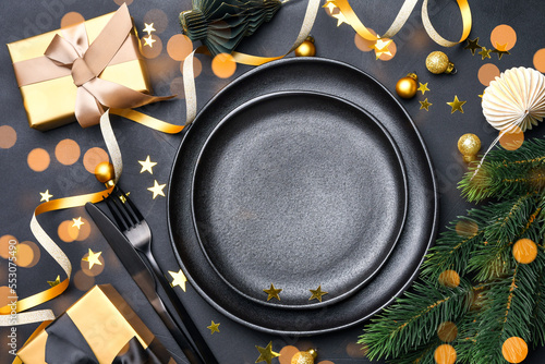 Festive New Year 2023 Christmas table setting black plates and gold decor on black Background, invitation dinner birthday party anniversary. copy space