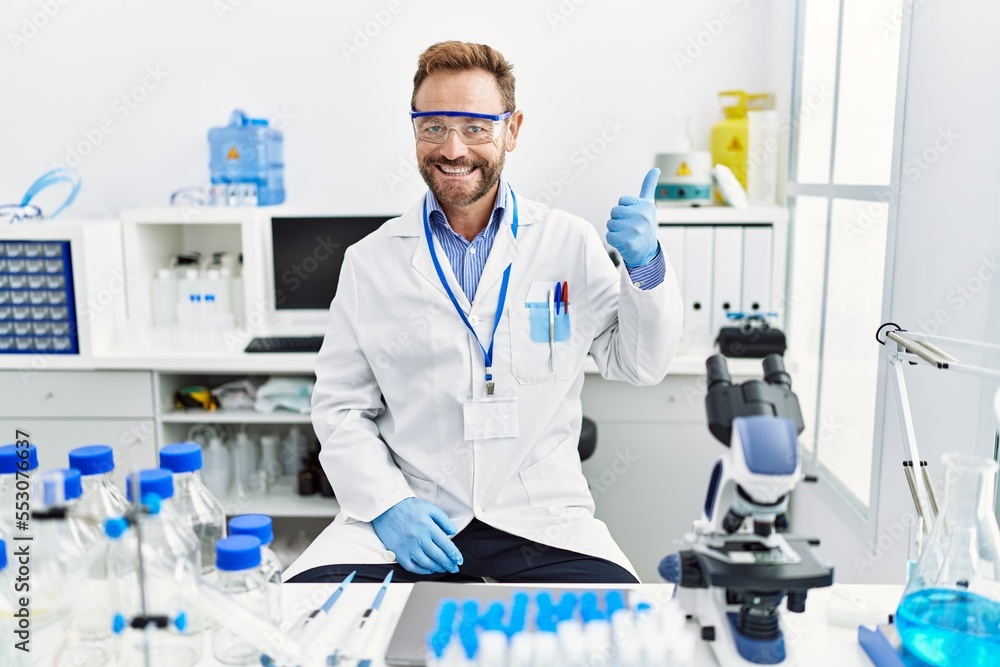 Middle age man working at scientist laboratory smiling happy and positive, thumb up doing excellent and approval sign Middle age man working at scientist laboratory smiling happy and positive, thumb up doing excellent and approval sign