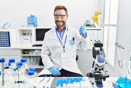 Middle age man working at scientist laboratory smiling happy and positive, thumb up doing excellent and approval sign