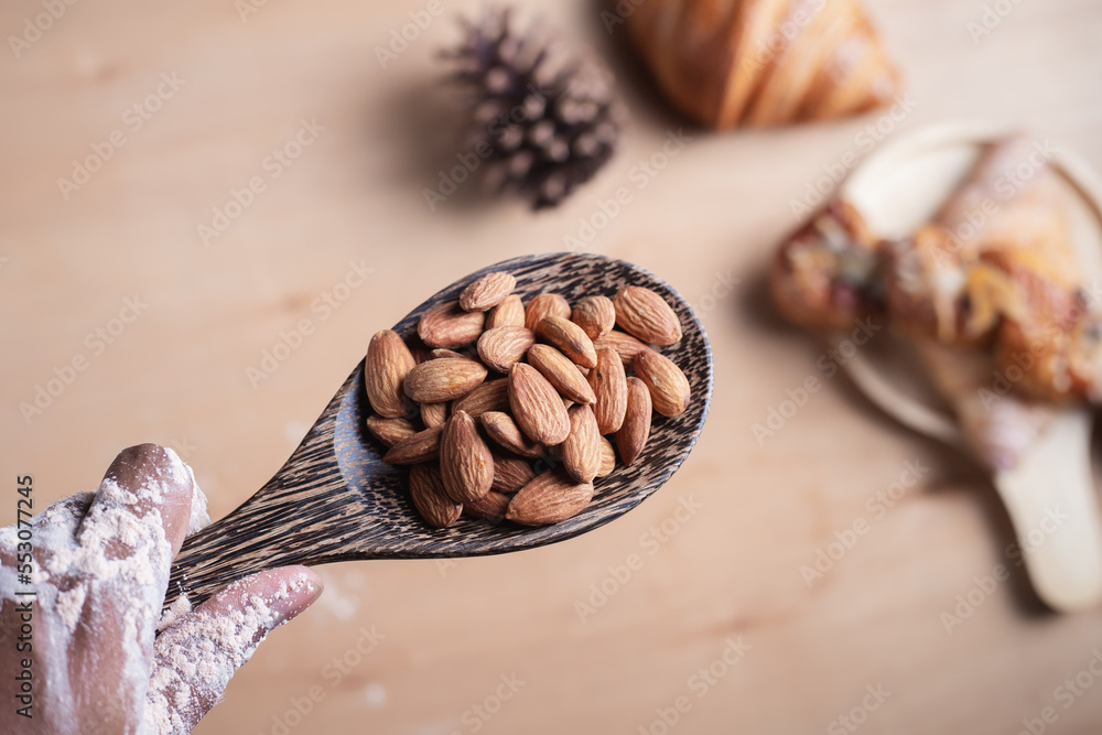 Closeup of almonds in wooden spoon with bread on wooden background, vintage tones, breadbread
