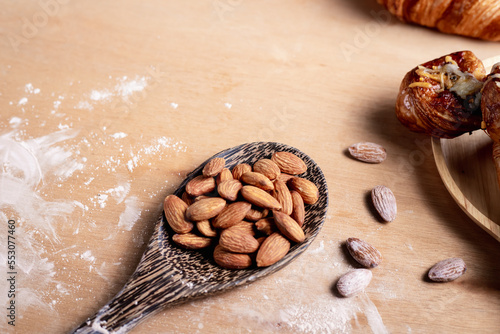 Closeup of almonds in wooden spoon with bread on wooden background, vintage tones, breadbread
 photo