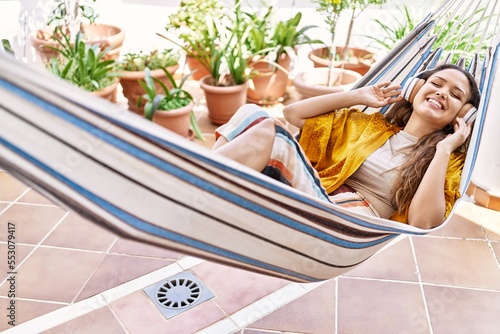 Young hispanic girl listening to music lying on hammock at the terrace.