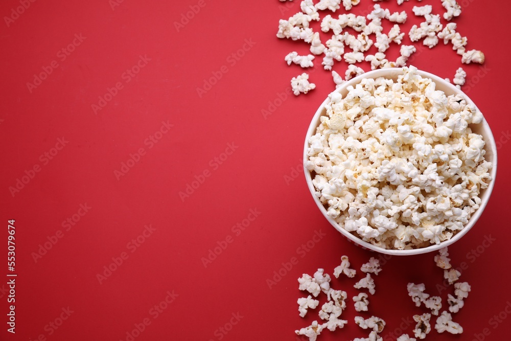 Paper bucket and delicious popcorn on red background, flat lay. Space for text Paper bucket and delicious popcorn on red background, flat lay. Space for text