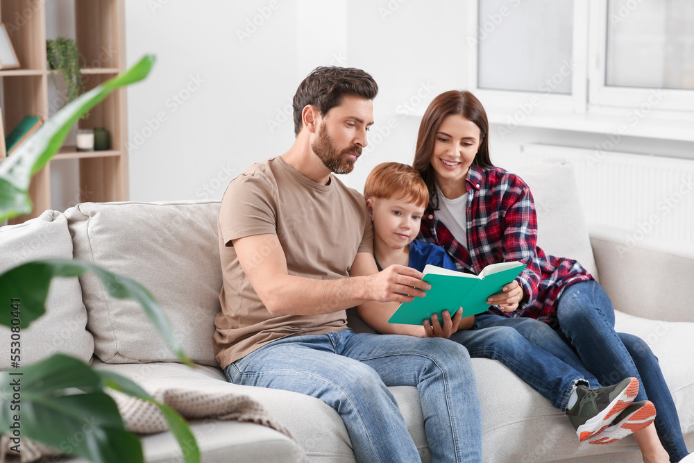 Happy parents with their child reading book on couch at home Happy parents with their child reading book on couch at home