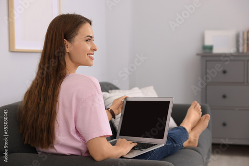 Happy young woman with laptop on sofa at home © New Africa