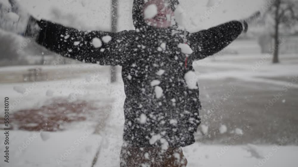 Young, happy, boy smiling and wearing a coat playing outside on a cold, winter day in December throws snow in the air during Christmas break in a small town in the midwest.