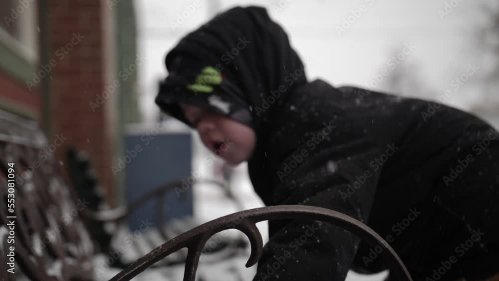 Young boy wearing a coat playing in the snow outside on a cold, winter day in December with a snow covered bench during Christmas break in a small town in the midwest. Young boy wearing a coat playing in the snow outside on a cold, winter day in December with a snow covered bench during Christmas break in a small town in the midwest.