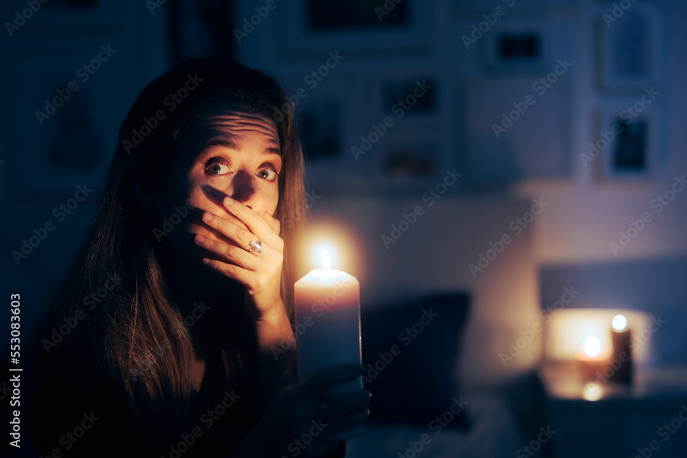 Stressed Woman Holding a Candle in Blackout No Power Situation. Unhappy person sitting in the dark at candlelight alone
Stressed Woman Holding a Candle in Blackout No Power Situation. Unhappy person sitting in the dark at candlelight alone