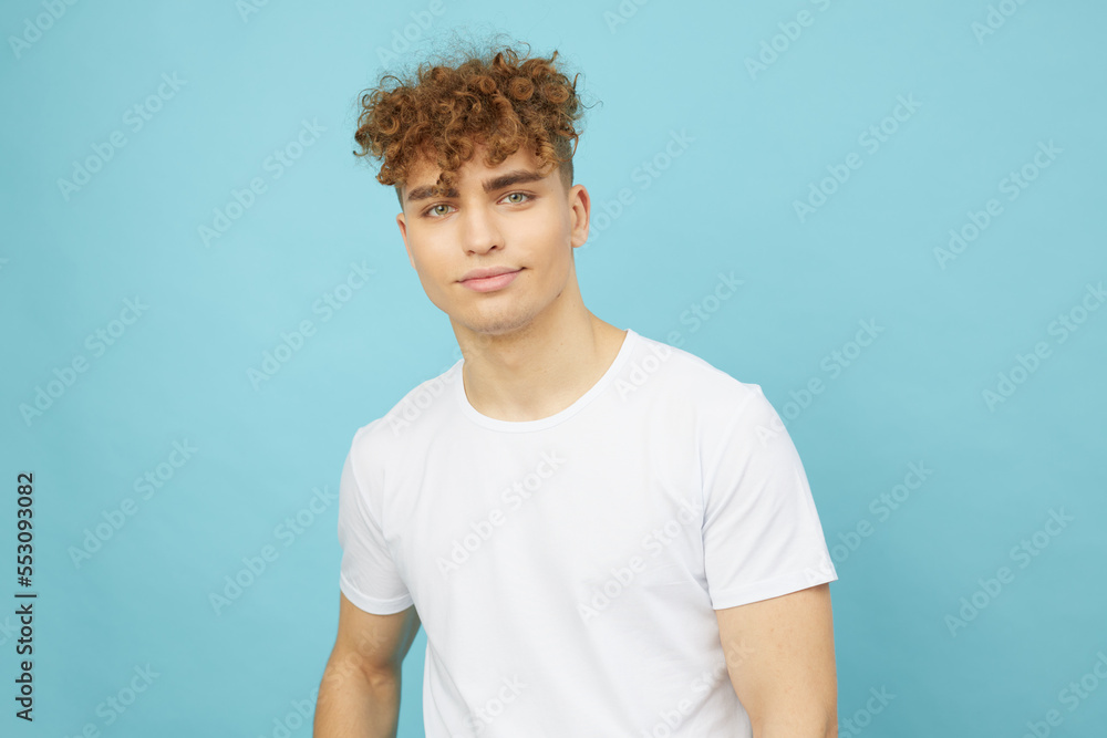a smiling, attractive young man with curly hair stands on a light blue background and looks into the camera smiling broadly. Photo with space for inserting an advertising layout a smiling, attractive young man with curly hair stands on a light blue background and looks into the camera smiling broadly. Photo with space for inserting an advertising layout