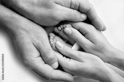 Legs, toes, feet and heels of a newborn. With the hands of parents, father, mother gently holds the child's legs. Macro photography, close-up. Black and white photo. High quality photo