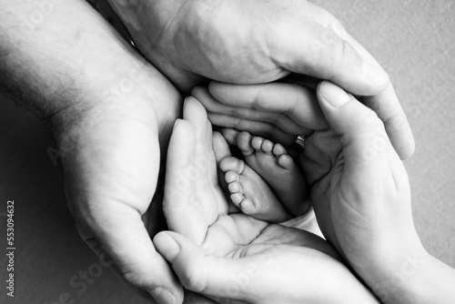 The palms of the parents. A father and mother hold the feet of a newborn child. 