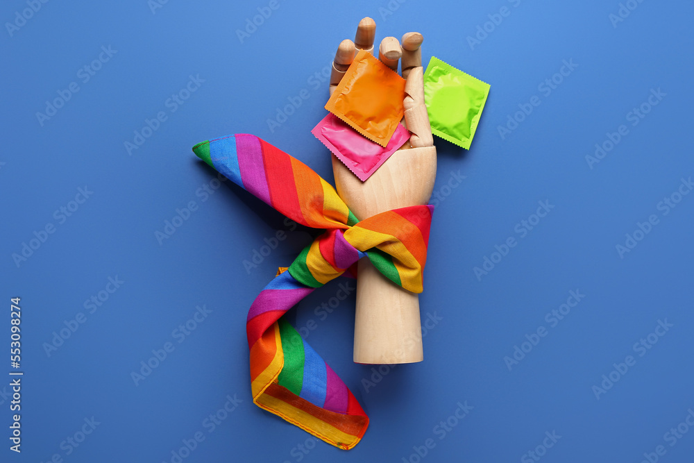 Wooden hand with condoms and rainbow scarf on blue background. Sex concept