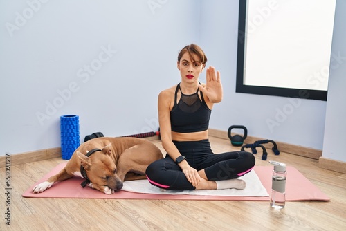 Young beautiful woman sitting on yoga mat doing stop sing with palm of the hand. warning expression with negative and serious gesture on the face.
