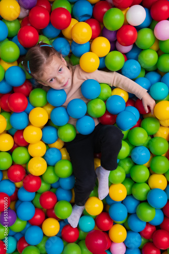 Cute little girl playing on multi coloured plastic balls in big dry paddling pool in playing centre. Having fun in playroom