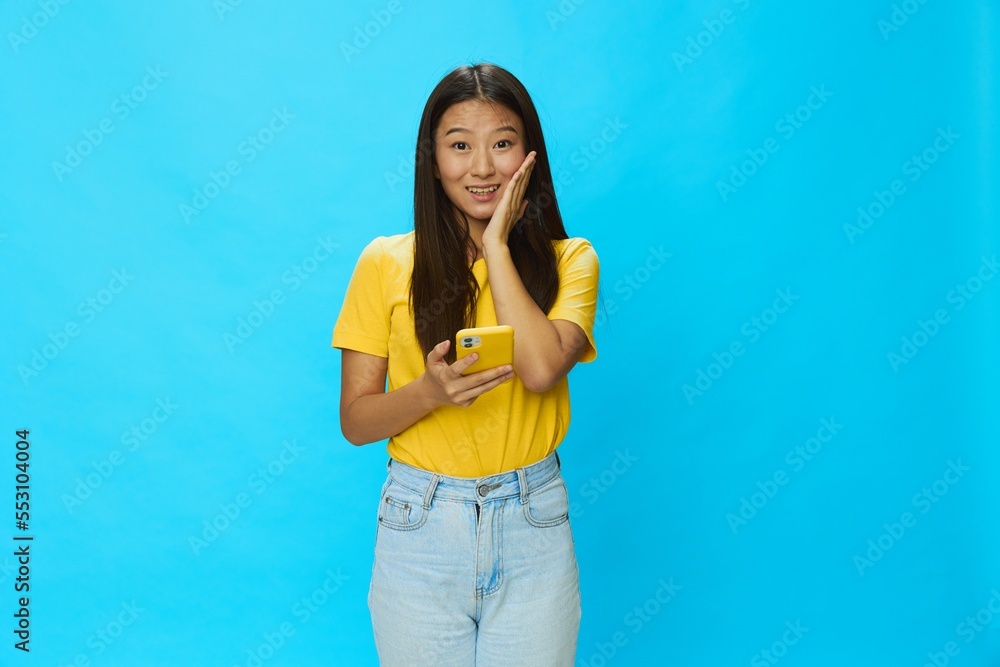 Happy Asian woman holding a phone with a yellow case on a blue background in a yellow T-shirt surprise Happy Asian woman holding a phone with a yellow case on a blue background in a yellow T-shirt surprise