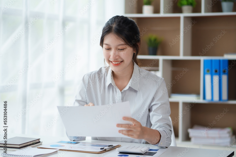 Attractive asian businesswoman sitting at work using laptop and examining many documents in office smiling. Attractive asian businesswoman sitting at work using laptop and examining many documents in office smiling.