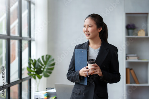 Beautiful Asian business woman standing smiling confident and bright looking ready to work in the new day with a cup of coffee. Please be ready to work.