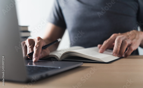 University student using laptop or computer for studying or learning book, reading textbook at home. Knowledge and skill training online at home. Education and cognition success idea concept