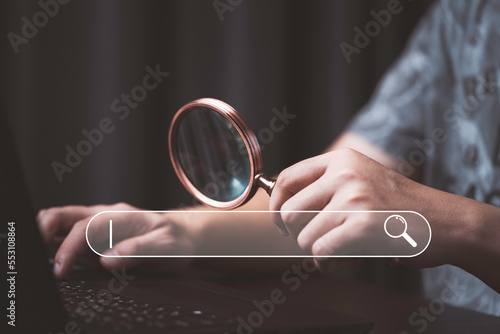 Man holding magnifier glass and using computer laptop with search bar icon for Search Engine Optimization or SEO concept to find information by internet connection.
