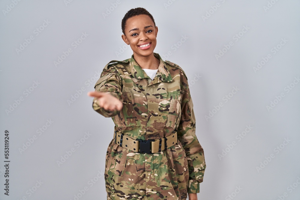 Beautiful african american woman wearing camouflage army uniform smiling cheerful offering palm hand giving assistance and acceptance.