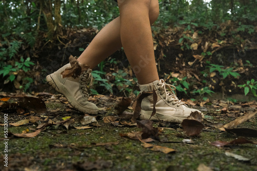 Young woman hiking in mountains or forest with trekking shoes. Concept of adventure, hiking and seasonal holidays with a side view of tourists on the trail.
