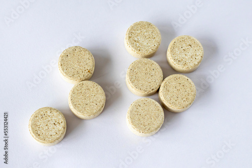 Supplements with chewable tablets DGL liquorice root. Round puck tablets of beige color with dark droplets on a white background view from above.