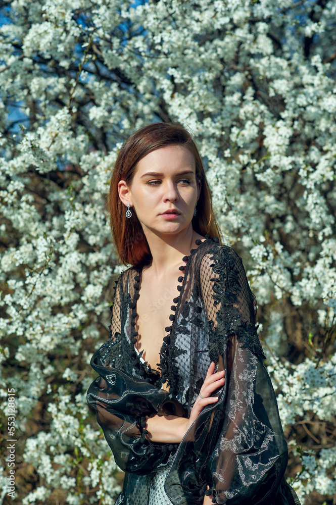 Portrait of a young beautiful girl in a spring blooming garden. Woman in an evening designer dress