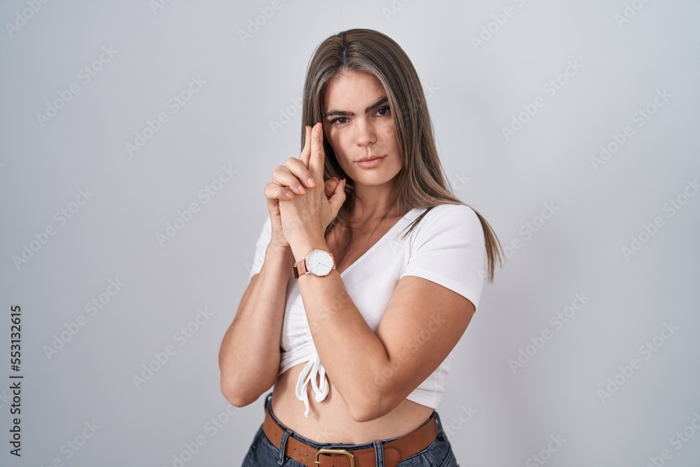 Young beautiful woman wearing casual white t shirt holding symbolic gun with hand gesture, playing killing shooting weapons, angry face Young beautiful woman wearing casual white t shirt holding symbolic gun with hand gesture, playing killing shooting weapons, angry face