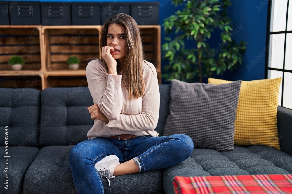 Beautiful woman sitting on the sofa at home looking stressed and nervous with hands on mouth biting nails. anxiety problem. Beautiful woman sitting on the sofa at home looking stressed and nervous with hands on mouth biting nails. anxiety problem.