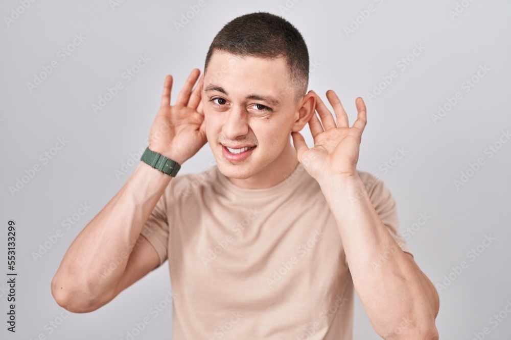 Young man standing over isolated background trying to hear both hands on ear gesture, curious for gossip. hearing problem, deaf Young man standing over isolated background trying to hear both hands on ear gesture, curious for gossip. hearing problem, deaf