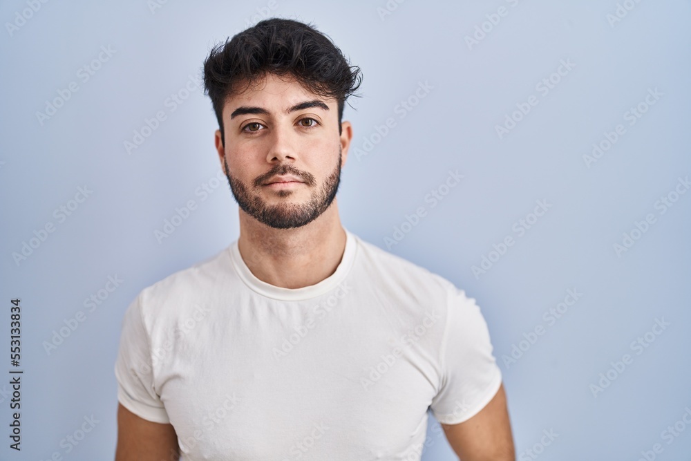 Hispanic man with beard standing over white background relaxed with serious expression on face. simple and natural looking at the camera. Hispanic man with beard standing over white background relaxed with serious expression on face. simple and natural looking at the camera.