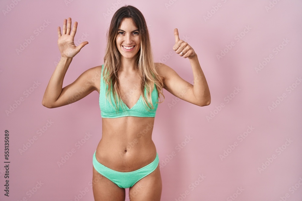 Young hispanic woman wearing bikini over pink background showing and pointing up with fingers number six while smiling confident and happy. Young hispanic woman wearing bikini over pink background showing and pointing up with fingers number six while smiling confident and happy.