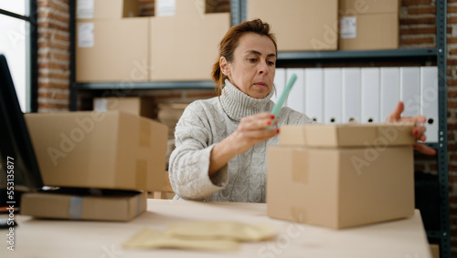 Middle age hispanic woman ecommerce business worker make photo to package at storehouse office