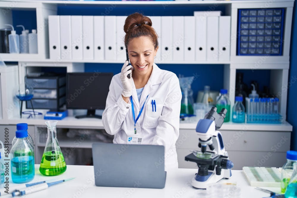 Young woman scientist talking on the smartphone using laptop at laboratory