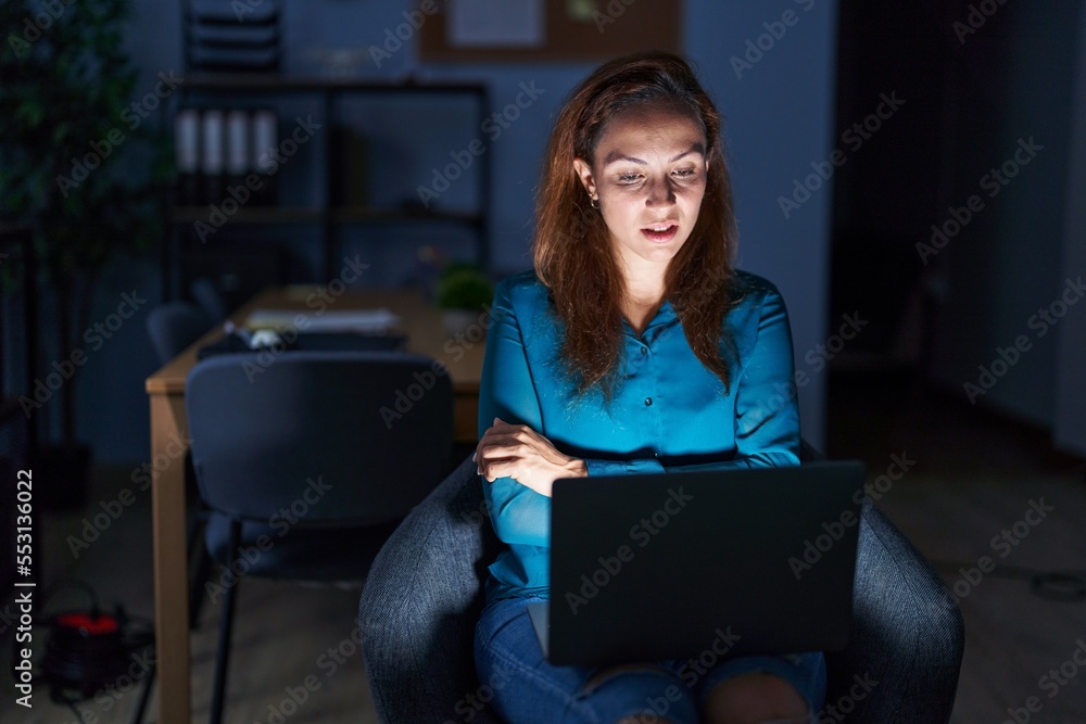 Brunette woman working at the office at night skeptic and nervous, disapproving expression on face with crossed arms. negative person. Brunette woman working at the office at night skeptic and nervous, disapproving expression on face with crossed arms. negative person.