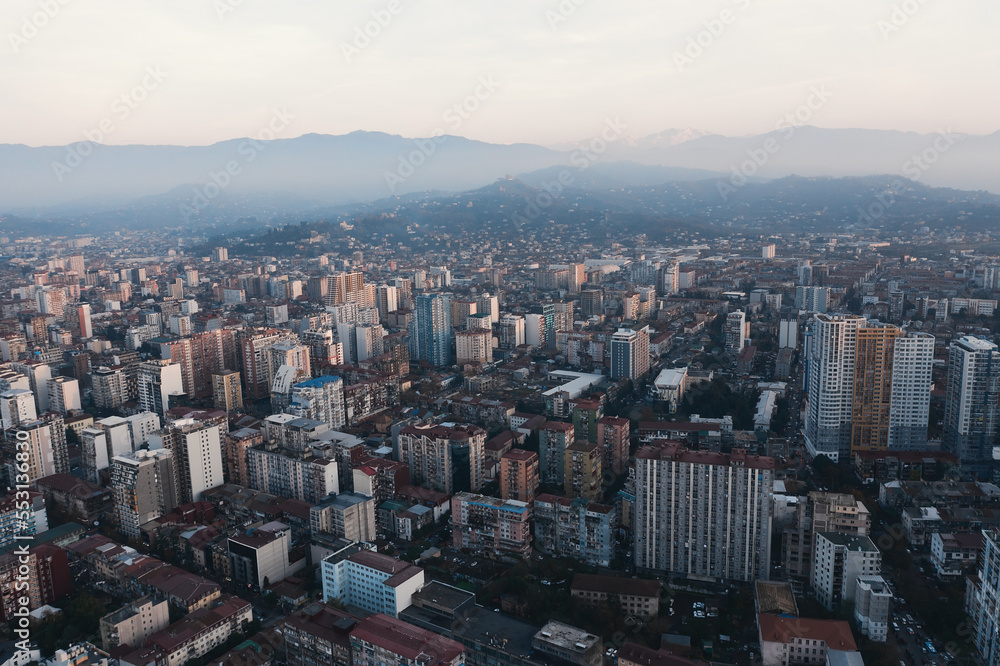 Aerial view from drone of evening panorama Batumi city buildings with mountains at background in twilight.