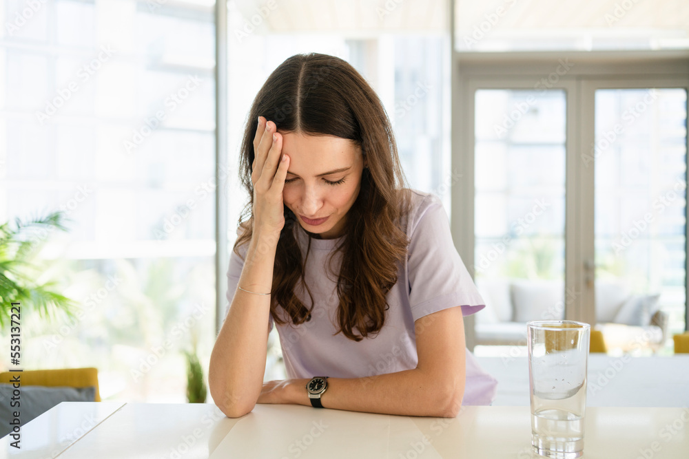 Stressed woman with head in hand leaning on table at home Stressed woman with head in hand leaning on table at home