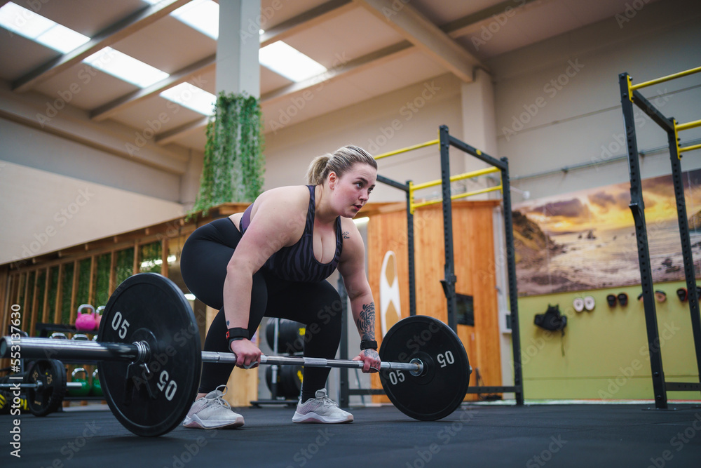 Confident overweight woman exercising with barbell in gym Confident overweight woman exercising with barbell in gym