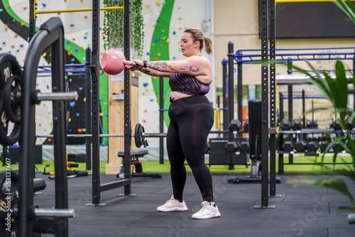 Young overweight woman working out with kettlebell in gym photo