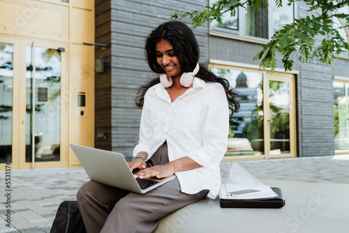 Young woman using laptop and headphones while studying outdoors