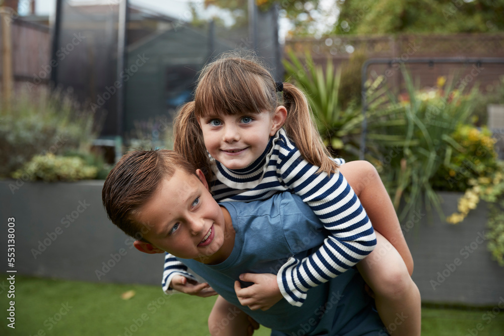 Smiling boy giving piggyback ride to sister in garden Smiling boy giving piggyback ride to sister in garden