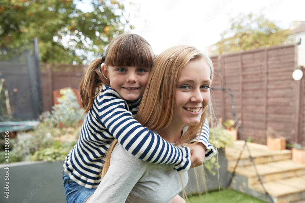 Smiling girl giving piggyback ride to sister in garden Smiling girl giving piggyback ride to sister in garden