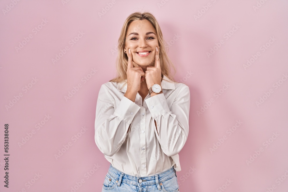 Young caucasian woman wearing casual white shirt over pink background smiling with open mouth, fingers pointing and forcing cheerful smile Young caucasian woman wearing casual white shirt over pink background smiling with open mouth, fingers pointing and forcing cheerful smile