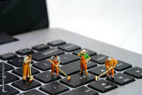 Miniature people toy figure photography. Group of sweeper workers cleaning notebook laptop keyboard using broom, brush. Isolated on white background