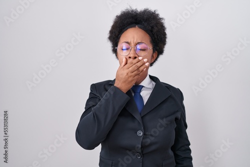 Beautiful african woman with curly hair wearing business jacket and glasses bored yawning tired covering mouth with hand. restless and sleepiness.