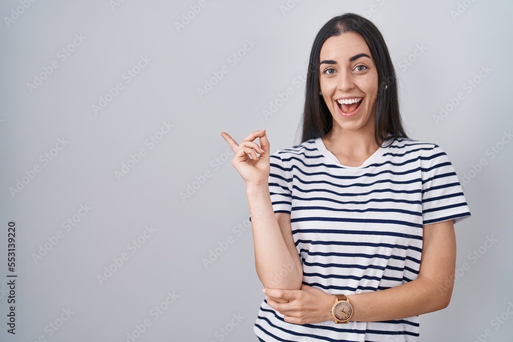 Young brunette woman wearing striped t shirt with a big smile on face, pointing with hand finger to the side looking at the camera. Young brunette woman wearing striped t shirt with a big smile on face, pointing with hand finger to the side looking at the camera.