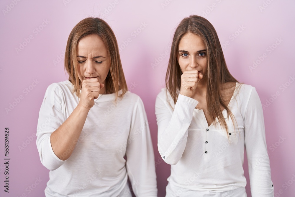 Middle age mother and young daughter standing over pink background feeling unwell and coughing as symptom for cold or bronchitis. health care concept.