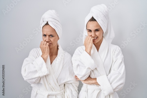 Middle age woman and daughter wearing white bathrobe and towel looking stressed and nervous with hands on mouth biting nails. anxiety problem.